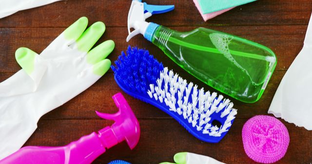 A variety of cleaning supplies, including spray bottles, gloves, sponges, and brushes, are laid out on a wooden surface, with copy space. These tools are essential for maintaining cleanliness and hygiene in domestic and professional environments.