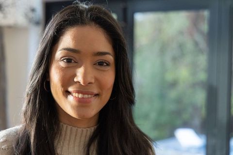Smiling woman wearing cream knit sweater and hoop earrings by sunlit glass doors