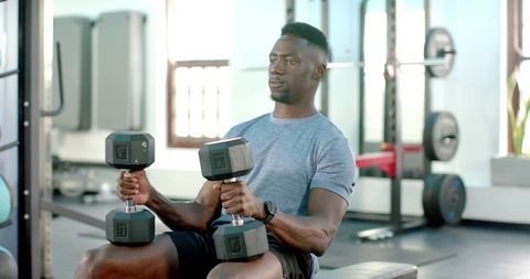 African American man performing seated dumbbell press in sunlit gym for strength training