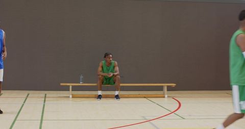 Sitting basketball player in green practice uniform resting on bench with water bottle