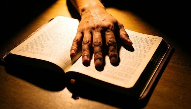 Hand pressing open book under warm light conveying devotion oath study reflection