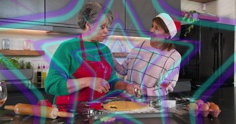 Holiday cookie baking: mature woman in red apron and friend in santa hat cutting dough