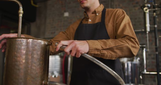 Caucasian man working at gin distillery, wearing apron, connecting pipe to distillation equipment. work at an independent craft gin distillery business.