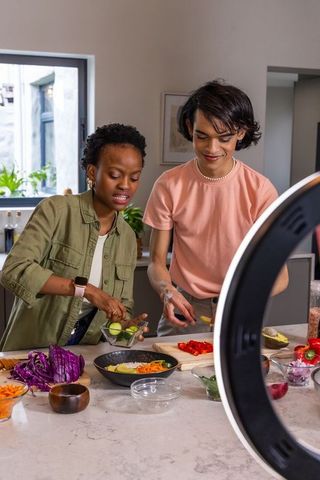 Diverse friends preparing colorful healthy bowl on marble countertop with ring light