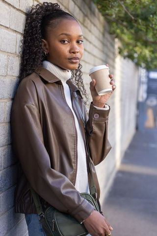 African american woman sipping coffee while leaning on brick wall urban street style portrait