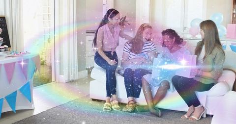 Group of friends celebrating newborn on sofa, holding baby and opening presents