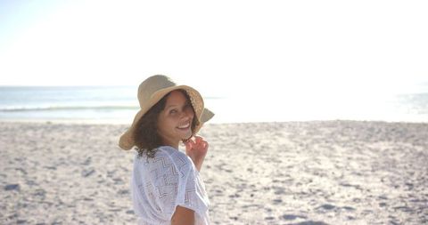 Woman on sunny beach in straw hat smiling with relaxed atmosphere