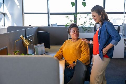 Diverse female coworkers collaborating in modern open-plan office, mentoring and support