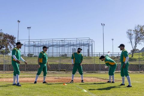 Baseball team practicing infield drill on sunny training field with batting cage, teamwork