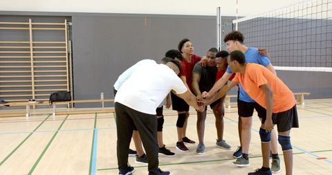 Diverse male volleyball team huddling for motivation on indoor court