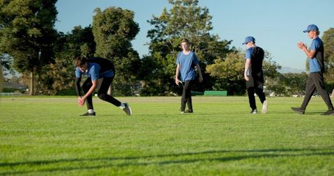 Teen cricket players bending, catching bright pink ball on sunny grassy field
