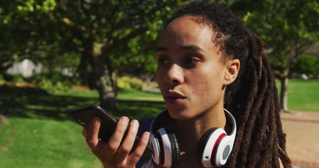 Young woman with headphones using smartphone voice command in park - Download Free Stock Images Pikwizard.com