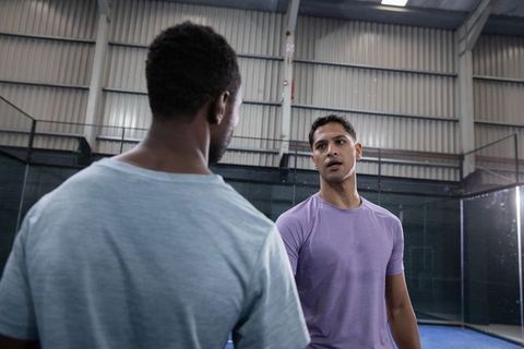 Diverse male players discussing strategy during indoor padel training on blue court