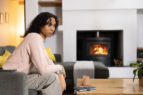 Nonbinary person relaxing by warm fireplace on cozy sofa with mug and notebook