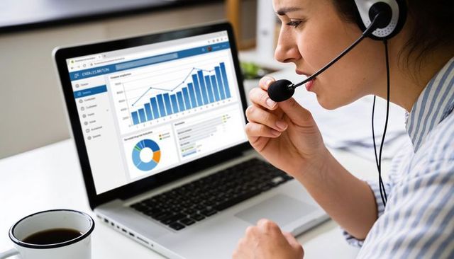 Customer service agent adjusting headset while reviewing analytics dashboard on laptop, remote work