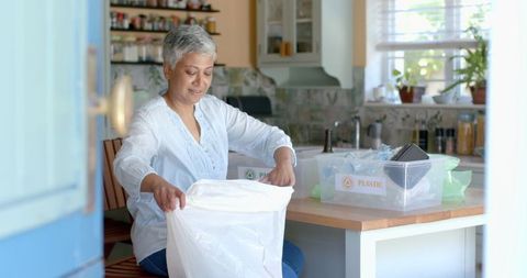 Senior Woman Sorting Household Waste for Recycling in Kitchen