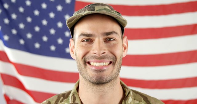 A smiling young Caucasian male in military uniform stands in front of an American flag, with copy space. His cheerful expression and the backdrop symbolize patriotism and service to the country.