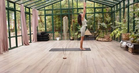 Woman Practicing Yoga Chair Pose in Glass House Surrounded by Greenery