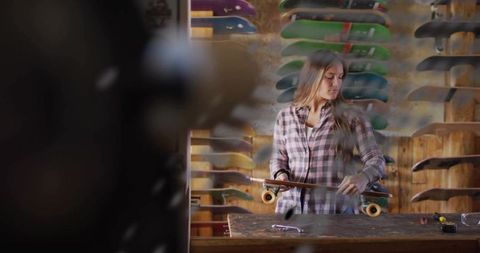 Woman Tightening Longboard Trucks in Skateboard Workshop Surrounded by Colorful Decks
