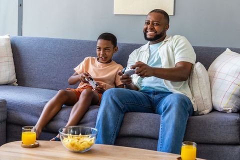 Black dad and son enjoying video game session on couch, home family bonding