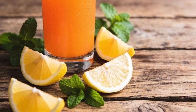 Refreshing orange drink with lemon wedges and mint on rustic wooden table closeup