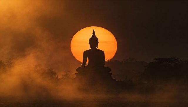 Seated buddha silhouette meditating against enormous sun halo over misty dawn temple