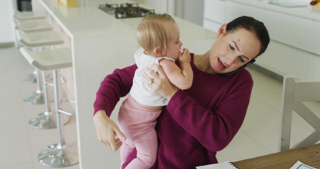 Caucasian mother holding her baby and talking on smartphone at home. motherhood, love and childcare concept