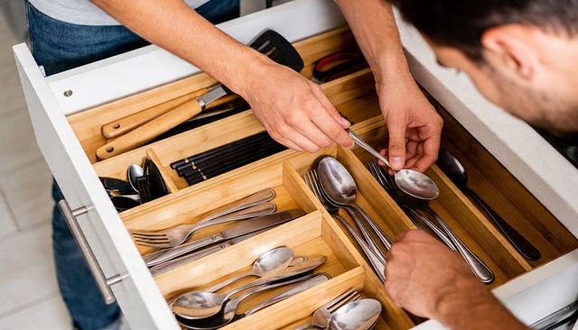 Couple sorting cutlery in bamboo drawer organizer, hands-on kitchen decluttering scene at home