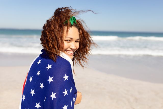 Biracial woman with curly brown hair is smiling at beach. She wears star-patterned cover-up, and ocean is in the background, unaltered