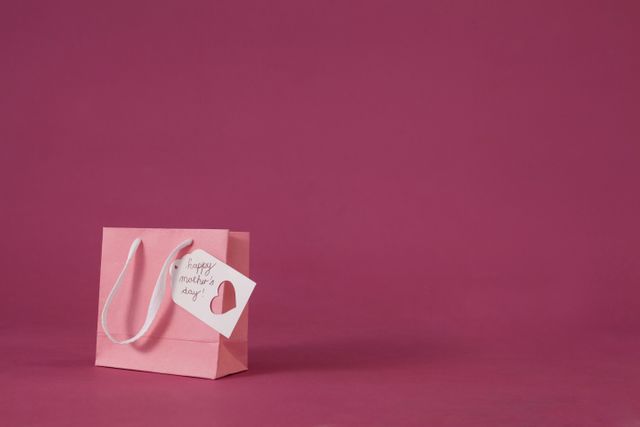 Pink gift bag with a heart-shaped tag and 'Happy Mother's Day' message. Ideal for Mother's Day promotions, greeting card designs, holiday advertisements, and social media posts celebrating mothers.