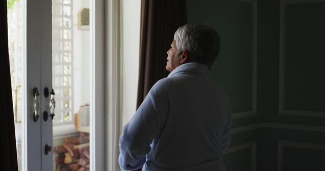 Senior Woman in Bathrobe Looking Out Window in Sunlit Room - Download Free Stock Images Pikwizard.com