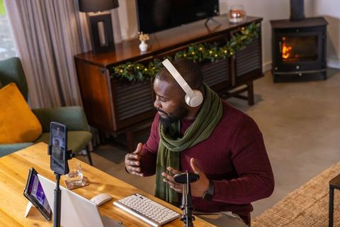 African american man recording podcast in cozy home studio wearing headphones and scarf