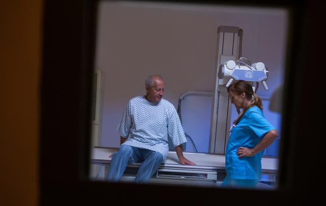 Elderly patient undergoing an x-ray examination in a hospital setting, with a medical professional assisting. Useful for healthcare, medical imaging, patient care, and diagnostic test themes.