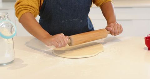 Home Baker Rolling Dough with Wooden Rolling Pin on Bright White Countertop