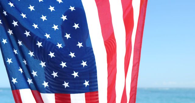 The American flag waving against the backdrop of a blue sky and ocean evokes a sense of patriotism and national pride. Perfect for use in articles, blogs, or advertisements related to American holidays, independence, or national pride. Ideal for promotional materials and educational purposes showcasing American heritage.