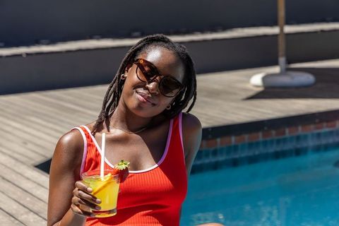 African american woman relaxing poolside in red swimsuit sipping tropical drink