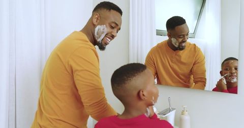 Father and son bonding time shaving together in bathroom mirror