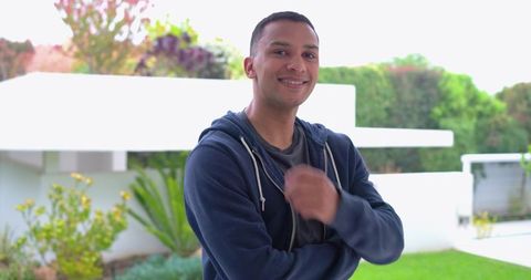 Confident young man standing in modern backyard wearing navy hoodie smiling casually