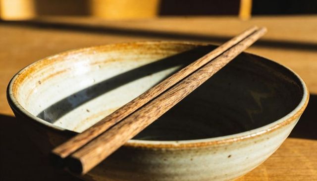 Rustic ceramic bowl with weathered wooden chopsticks resting on sunlit wooden surface