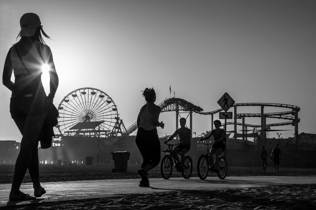 People enjoying a sunset at a beach boardwalk with amusement rides in the background. Ideal for themes of relaxation, summer fun, outdoor adventure, and urban landscapes.