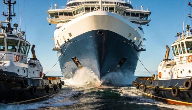 Tugboats guiding massive cruise ship bow through harbor channel creating powerful wake