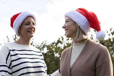 Middle-aged friends wearing santa hats smiling and chatting in sunny garden holiday scene