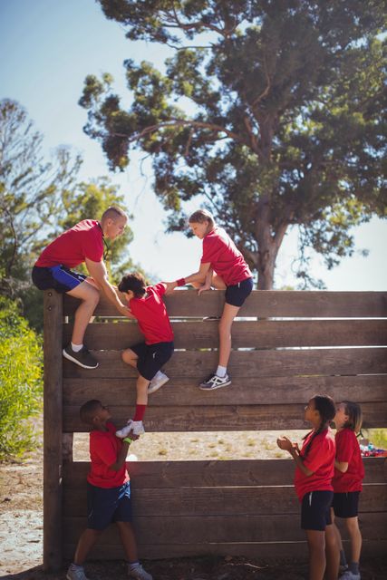 Trainer assisting kids to climb a wooden wall during obstacle course training at boot camp