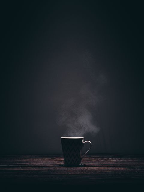 Steaming coffee mug making subtle waves as it sits on dark wooden table. Dark, minimalistic background highlighting sense of tranquility and simplicity. Useful for promoting cafes, coffee products, minimalist lifestyle blogs, or evoking morning routines and cozy moments in advertising.