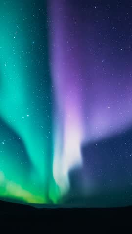 Vertical aurora borealis video showing green curtains intertwining with purple ribbon over hills