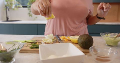 Female squeezing lemon over egg avocado toast on wooden board in modern home kitchen