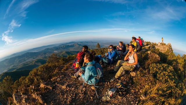 Group hiking team resting on mountain ridge at golden hour with panoramic valley vista