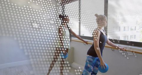 Practicing barre workout holding blue fitness balls by sunlit window with dotted light