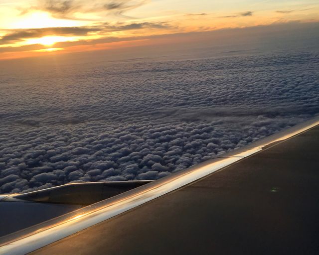 Scenic sunset above clouds captured from airplane window, showcasing the sky turning golden with dark cloud cover below. Perfect for themes of travel, aviation, adventure, and beauty in nature.