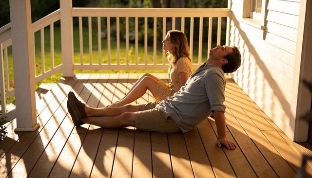Couple relaxing on sunlit porch leaning back and gazing during golden hour, warm shadows on deck